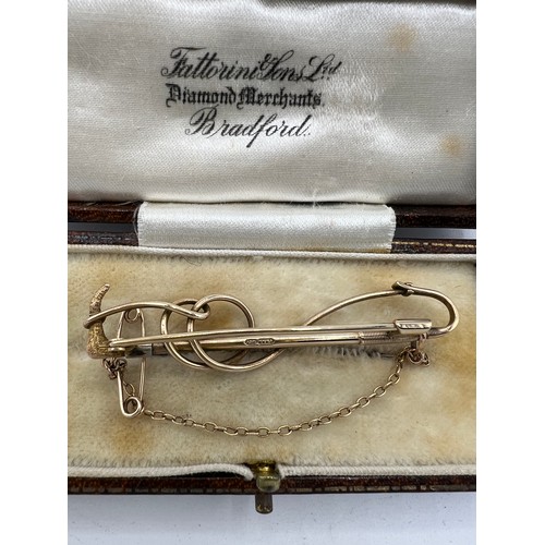 475 - A nine carat gold bar brooch in the form of a riding crop with safety chain, in fitted presentation ... 