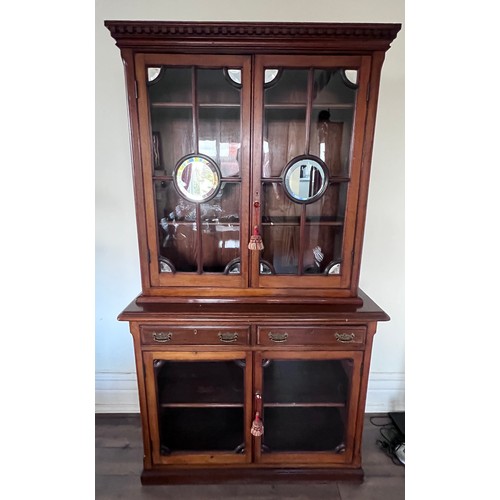 110 - A double height mahogany display/bookcase. Two glazed doors to top with mirrored roundels and corner... 