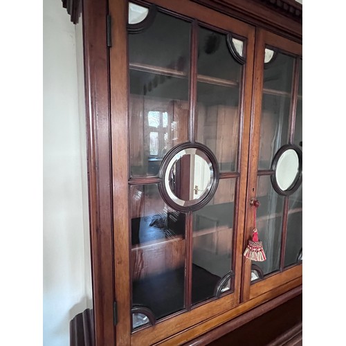 110 - A double height mahogany display/bookcase. Two glazed doors to top with mirrored roundels and corner... 