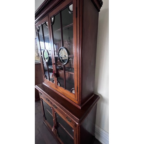 110 - A double height mahogany display/bookcase. Two glazed doors to top with mirrored roundels and corner... 