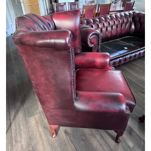 112 - A red leather suite comprising three seater Chesterfield together with wing armchair and low backed ... 