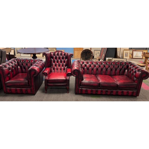 112 - A red leather suite comprising three seater Chesterfield together with wing armchair and low backed ... 