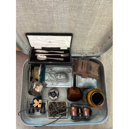 1306 - A vintage suitcase and contents to include wooden tank money box dated 1946, opera glasses, metal mu... 