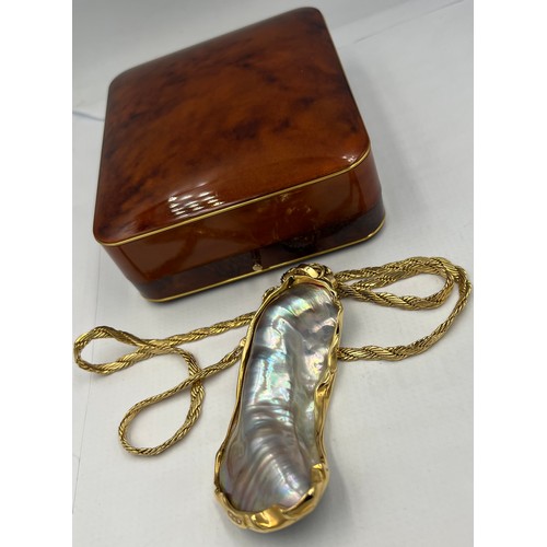 688 - A mother of pearl shell mounted in unmarked yellow metal on an unmarked yellow metal chain.