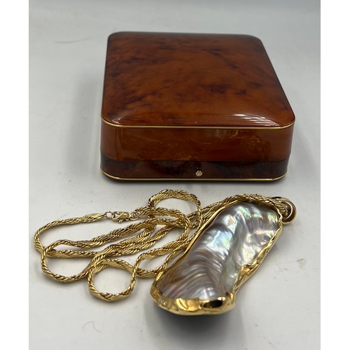 688 - A mother of pearl shell mounted in unmarked yellow metal on an unmarked yellow metal chain.