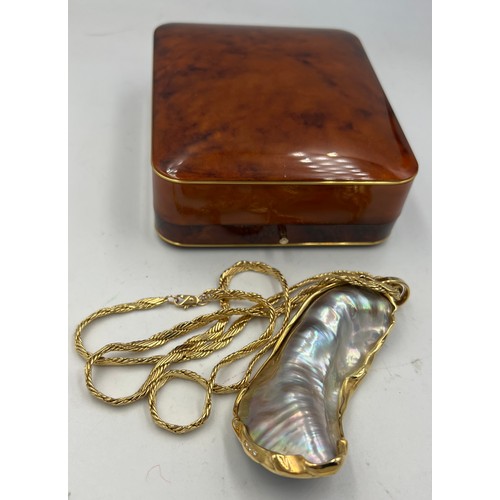 688 - A mother of pearl shell mounted in unmarked yellow metal on an unmarked yellow metal chain.