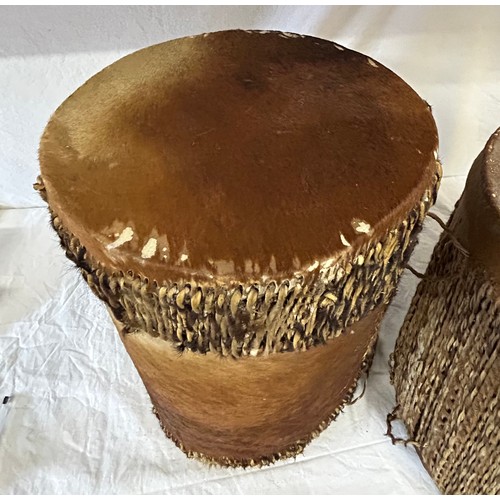 981 - Two traditional African cow hide drums. Tallest 42cm x 26cm, other 36cmx31cm. Rush decoration to edg... 