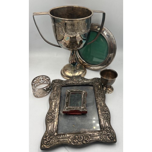 798 - Hallmarked silver to include three photograph frames, egg cup, napkin ring and NSPCC presentation cu... 