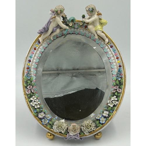 1233 - A Continental porcelain vanity easel mirror with applied cherub and floral decoration and bevelled g... 