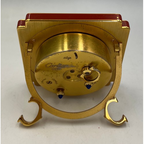 1000 - A Cartier Paris metal and red cased travelling alarm clock, the white circular dial having black Rom... 