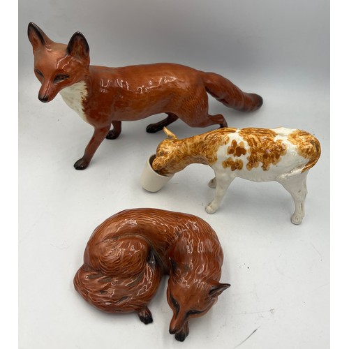 164 - Two Beswick foxes, a standing fox approx. 22cm w x 13cm h, a curled fox No 1017 together with a cera... 