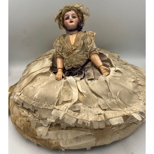 1324 - A bisque headed half doll with real hair and blue glass eyes attached to a silk covered tea cosy. He... 