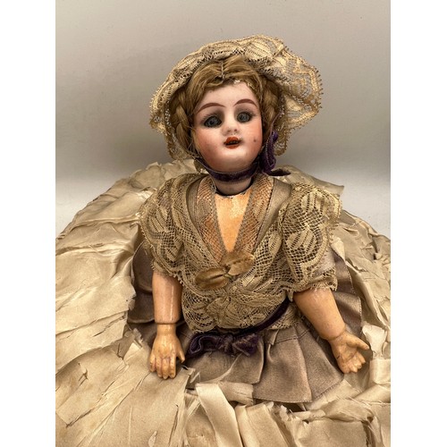 1324 - A bisque headed half doll with real hair and blue glass eyes attached to a silk covered tea cosy. He... 