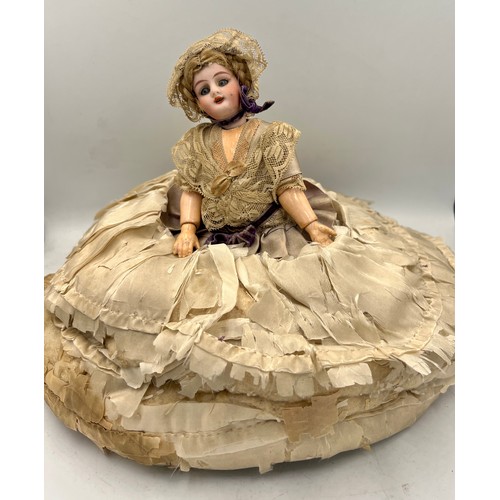 1324 - A bisque headed half doll with real hair and blue glass eyes attached to a silk covered tea cosy. He... 