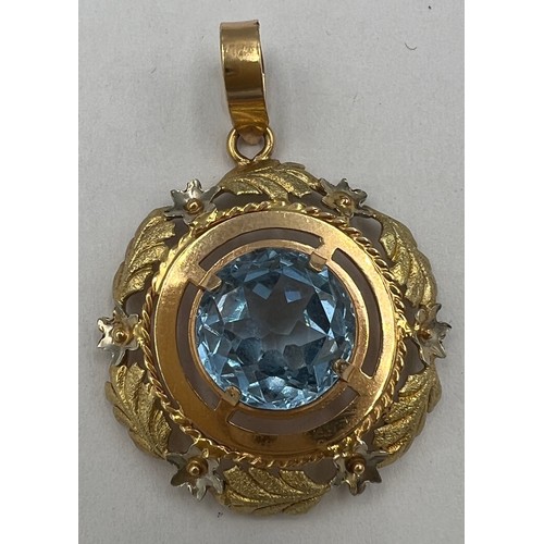 602 - A 18 carat yellow gold circular pendant with leaf decoration and set with a central pale blue stone.... 