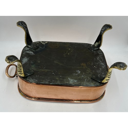 969 - A 19thC copper pan raised on four lions paw feet with drop handles. 45cm l x 32cm w x 22cm h.