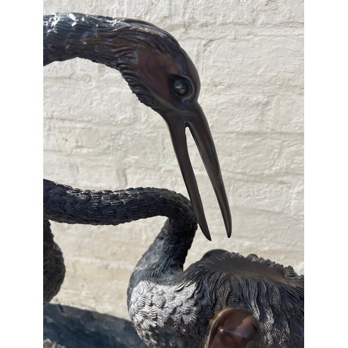 1052 - A pair of Japanese bronze cranes on later marble base. Height 132cm.