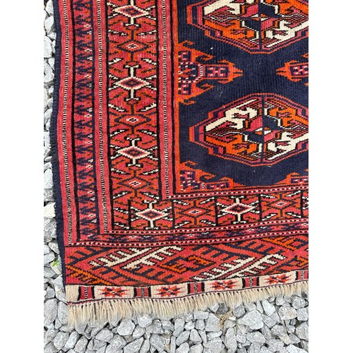 1289 - A 20thC hand knotted floor rug, red ground with blue geometric design and tassels. 140 x 104cm.