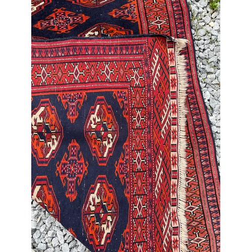 1289 - A 20thC hand knotted floor rug, red ground with blue geometric design and tassels. 140 x 104cm.