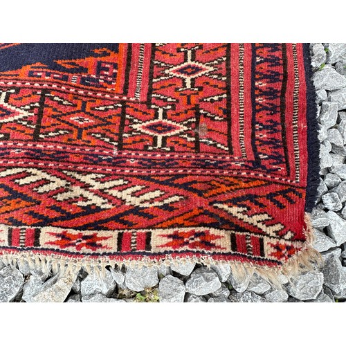 1289 - A 20thC hand knotted floor rug, red ground with blue geometric design and tassels. 140 x 104cm.