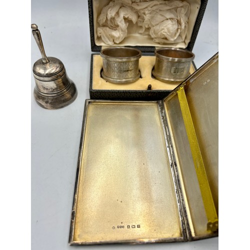 884 - Hallmarked silver to include cigarette case, napkin rings and a .925 silver bell. Total weight 288gm... 