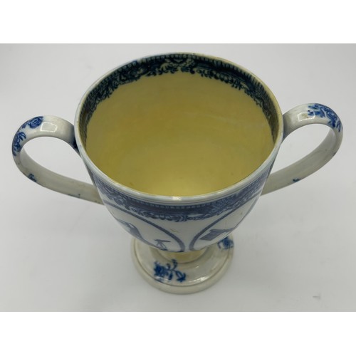 265 - An early 19th century blue and white transfer-printed loving cup, c. 1815. It has four vignettes wit... 