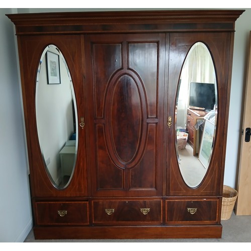 143 - An Edwardian mahogany wardrobe with oval mirrored doors to either side and three drawers to base. 19... 