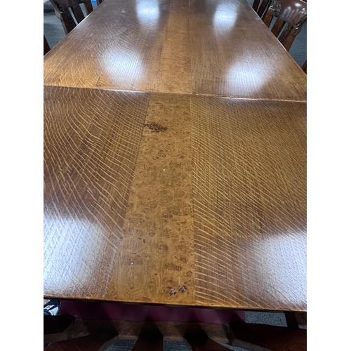 103 - An early 20thC Arts and Crafts style oak and burr walnut panels expanding dining table with eight ch... 