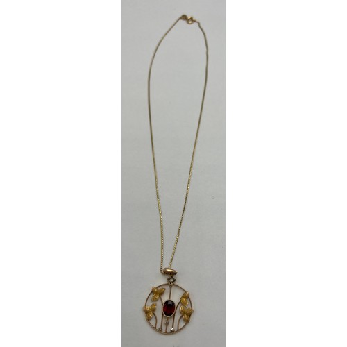 20 - A nine carat gold pendant set with central garnet and seed pearls suspended on an 18 carat gold chai... 