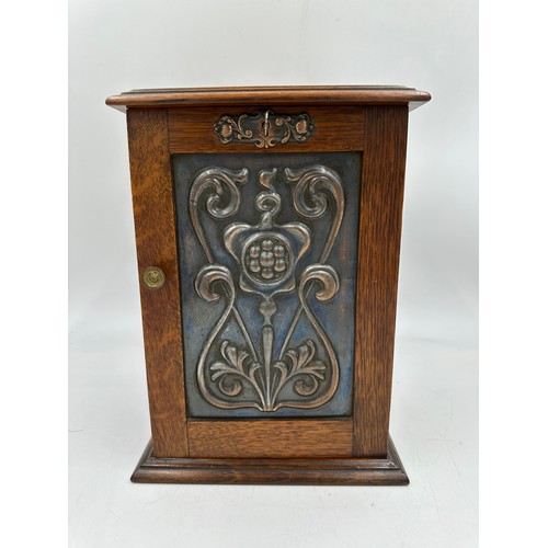 900 - An Arts and Crafts oak smokers cabinet with embossed metal decoration to door, containing 3 x pipes ... 