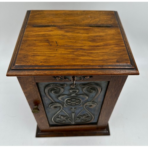 900 - An Arts and Crafts oak smokers cabinet with embossed metal decoration to door, containing 3 x pipes ... 