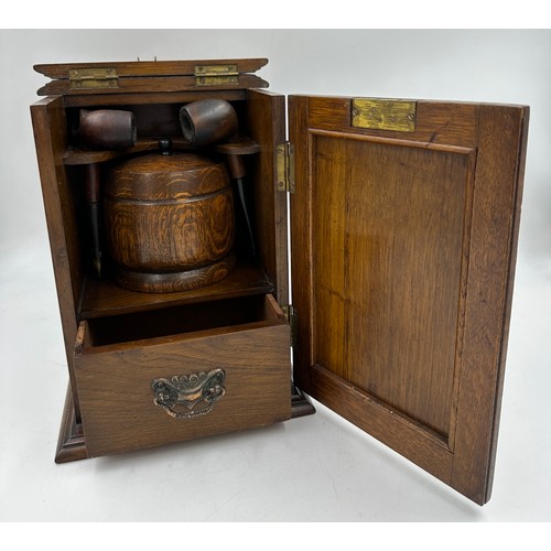 900 - An Arts and Crafts oak smokers cabinet with embossed metal decoration to door, containing 3 x pipes ... 