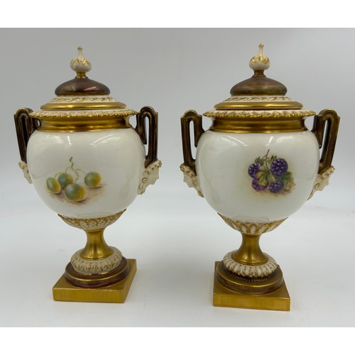 376 - A pair of Royal Worcester twin handled lidded urns with masks to sides on a circular foot with a squ... 