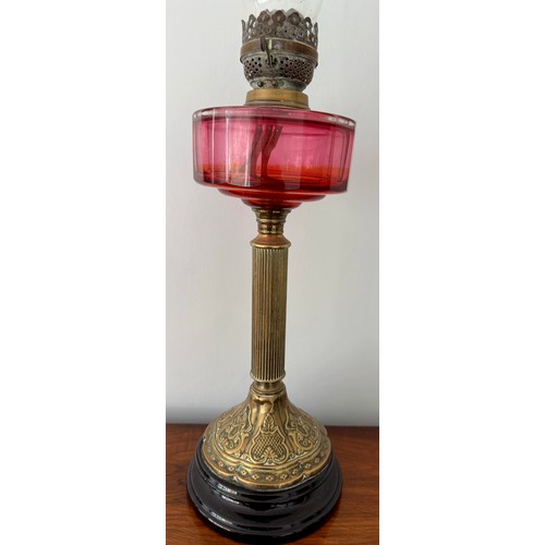 979 - A 19thC cranberry and brass oil lamp with black ceramic base. 48cm h to fitting.