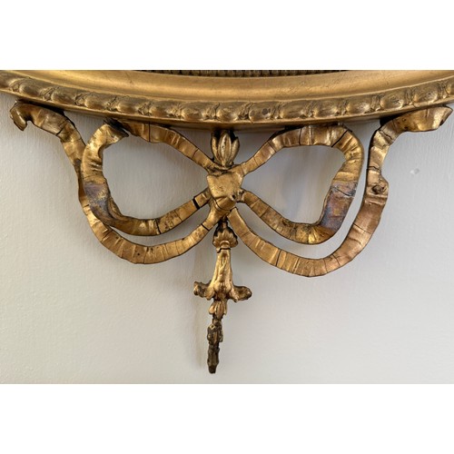 1029 - A gilt framed bevel edged oval wall mirror with decorative bows and swags. 61 w x 81cm h.