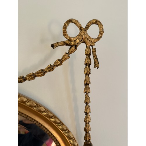 1029 - A gilt framed bevel edged oval wall mirror with decorative bows and swags. 61 w x 81cm h.