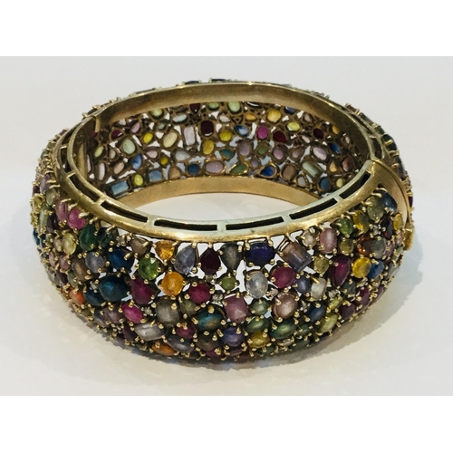 201 - A 9ct yellow gold wide hinged bangle, encrusted with a variety of multi coloured gemstones including... 