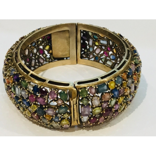 201 - A 9ct yellow gold wide hinged bangle, encrusted with a variety of multi coloured gemstones including... 