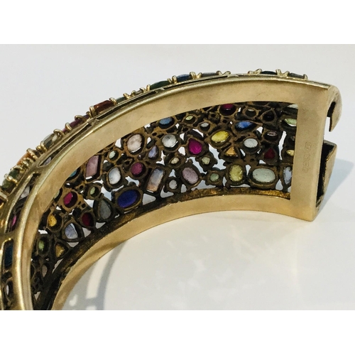 201 - A 9ct yellow gold wide hinged bangle, encrusted with a variety of multi coloured gemstones including... 