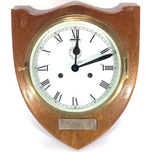 436 - A ship’s brass bulkhead clock with white enamel dial and black numerals, mounted on wooden shield wi... 