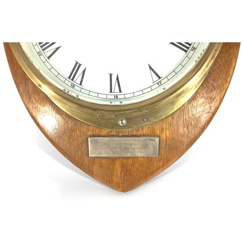 436 - A ship’s brass bulkhead clock with white enamel dial and black numerals, mounted on wooden shield wi... 