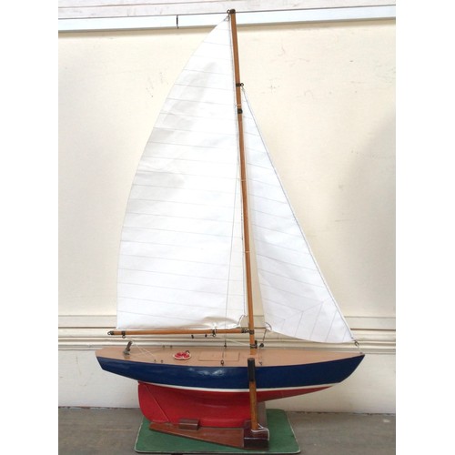 438 - A small pond yacht with hull painted red, white and blue, and white sails, raised on wooden stand,  ... 