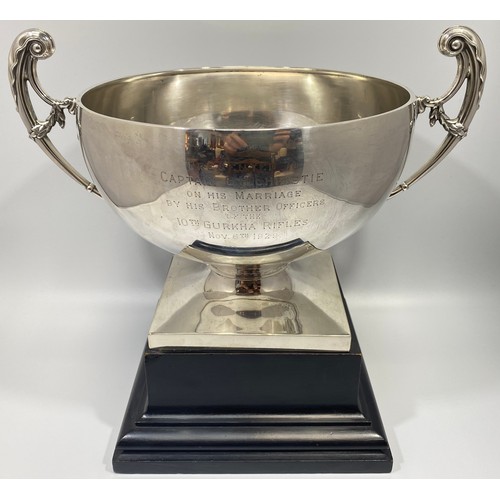 72 - A large silver trophy bowl by Mappin & Webb, with twin scrolled, floral handles and raised on square... 