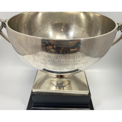 72 - A large silver trophy bowl by Mappin & Webb, with twin scrolled, floral handles and raised on square... 