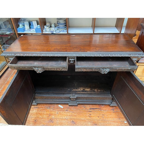 554 - A Victorian carved 'pussy' oak sideboard / cabinet with carved frieze above a pair of drawers with g... 