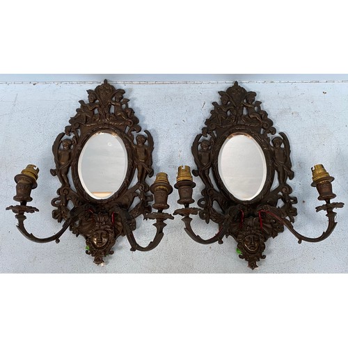 475 - A pair of French bronze twin-branched wall sconces, central oval mirrored panels surrounded by cheru... 