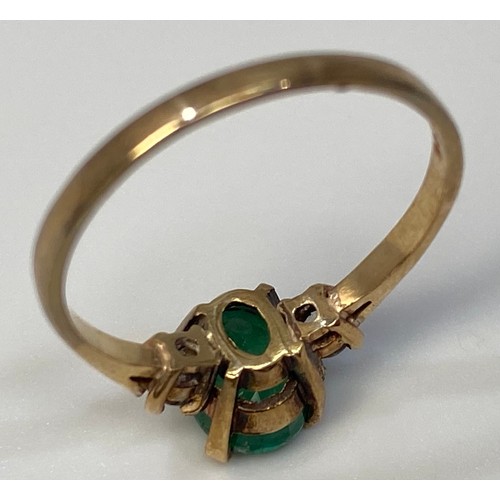 276 - A 9ct gold ring centrally four claw set with an oval, faceted emerald coloured stone, flanked by two... 