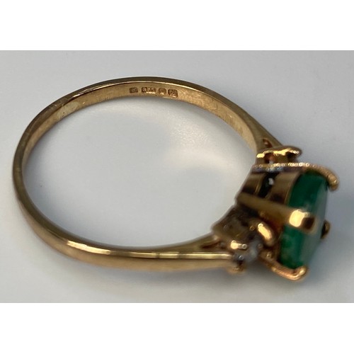 276 - A 9ct gold ring centrally four claw set with an oval, faceted emerald coloured stone, flanked by two... 