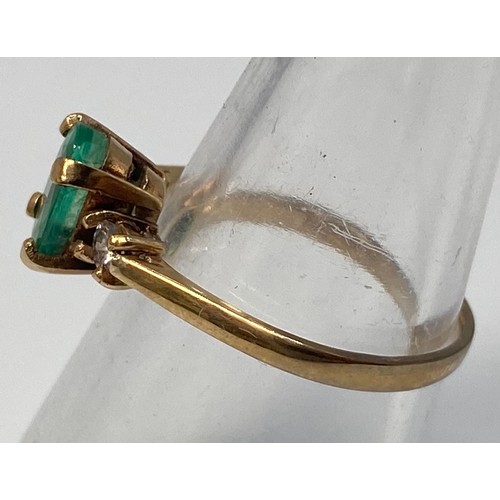 276 - A 9ct gold ring centrally four claw set with an oval, faceted emerald coloured stone, flanked by two... 