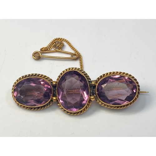 218 - A yellow metal (tests as 14 or 15ct) brooch set with three oval faceted amethyst coloured stones in ... 